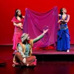 Duas mulheres seguram um vem que separam uma terceira mulher e um homem que conversam sentados ao chão